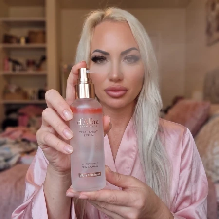 Kobieta trzymająca w dłoniach dwufazowe serum w sprayu d'Alba Vital z widoczną różową fazą olejową.
